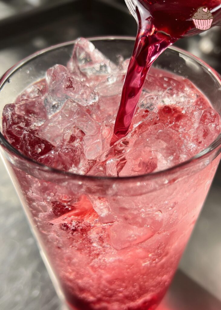 A tall glass of vibrant raspberry dream dirty soda with fresh raspberries and a straw.